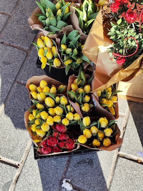 A collection of fresh flower bouquets placed on an outdoor tiled surface, featuring vibrant yellow tulips with closed buds and green stems, alongside bright red tulips with slightly open petals. The f
