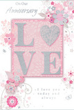 This anniversary card is shown closed, its front design creating an intimate, romantic scene that feels right at home in Shepherd's Bush. The dominant feature is the word LOVE, written in raised, softly glittered letters that shimmer in silver tones and invite gentle touch. The letter O has been transformed into a gleaming heart, textured and slightly domed so it seems to glow from within, like a small jewel set into the card. Surrounding this centrepiece is a graceful halo of delicate blossoms and winding vines, all illustrated with fine, flowing lines that curl and loop in a natural rhythm, recalling the curves of stems in a hand-crafted bouquet. The flowers are kept in a palette of pastel pinks, mauves, pearly whites, and understated greys, giving an effect similar to a soft spring garden after rain, perhaps like the calm pockets of green found behind the busy streets near Shepherd's Bush Market. Some petals appear as though gently washed in watercolour, their edges diffused into the blush background, while others are accented with hints of silver that sparkle discreetly. Tiny flourishes-minute petals, swirling scrolls, and subtle butterflies-add a sense of movement and joyful celebration without crowding the design. The phrases On Our Anniversary and I love you today and always are written in an elegant script and refined typeface, balancing the decorative artwork with heartfelt clarity. Altogether, the card feels like a quiet, deeply personal keepsake, perfectly suited to accompany a same-day anniversary flower delivery across Shepherd's Bush, carrying with it a whisper-soft yet powerfully sincere message of lasting love.